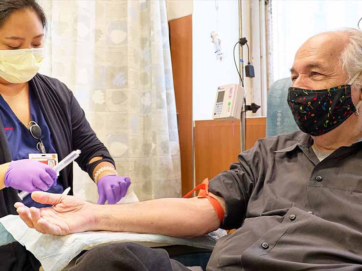 Michael Toomey sitting in a chair as an infusion nurse prepares to start his IV drop for the alzheimer's infusion drug lecanemab.